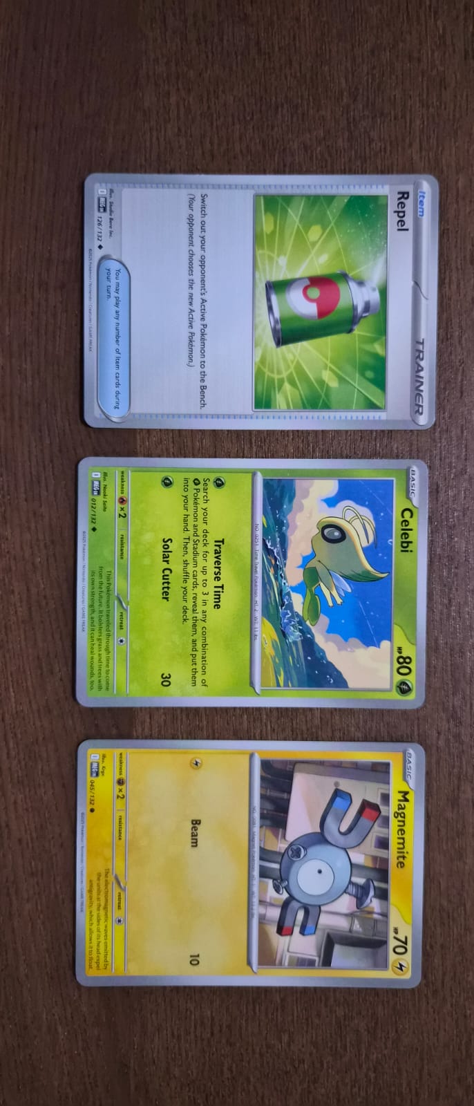 Three Pokémon trading cards laid out on a wooden table.